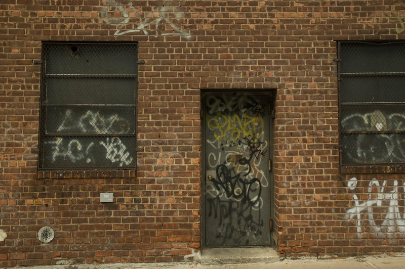 A brick building with a steel door, covered in graffiti.