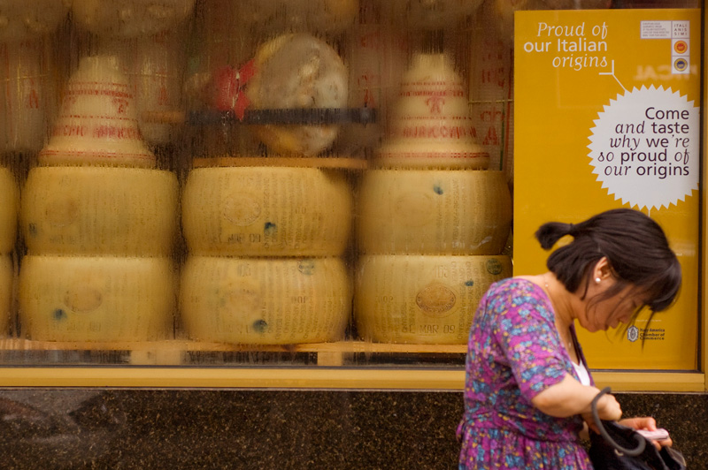 A Chinese-American woman fumbles with her cell phone in front of an Italian gourmet food shop.
