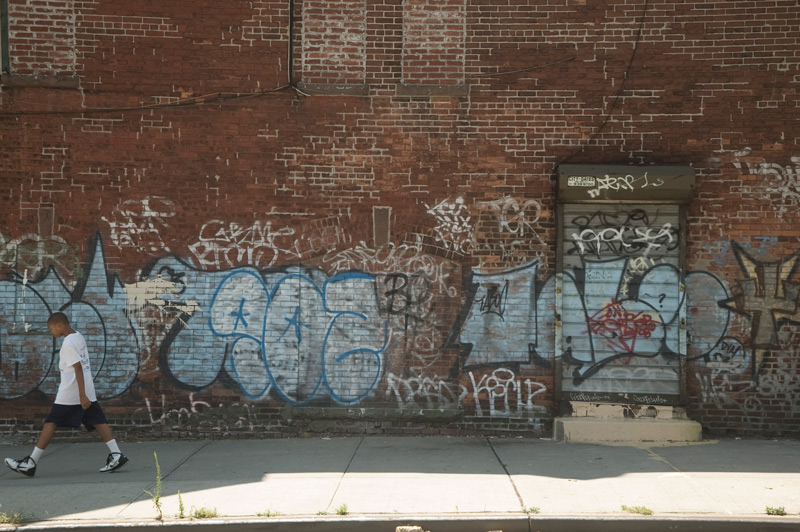 A youth walks past a brick wall covered in inartistic tags.