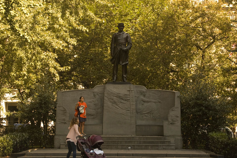 A statue on a monument, with a woman admiring a building in the distance