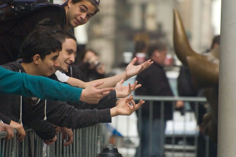 Tourists jokingly stretch to reach the bronze bull in New York's financial district.