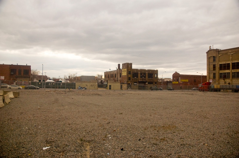 A large empty lot, with large buildings in the distance.
