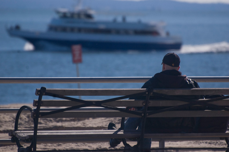 A retiree on a bench watches a boat pass by.