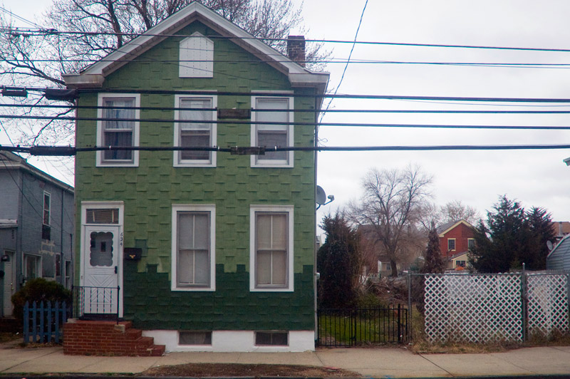 A small, green home, with above ground wires.