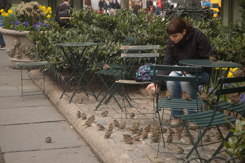 A young woman feeding sparrows in a park.