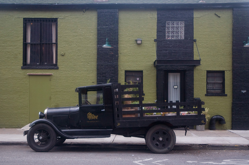 A green brick building, with an old black pickup truck parked in front.