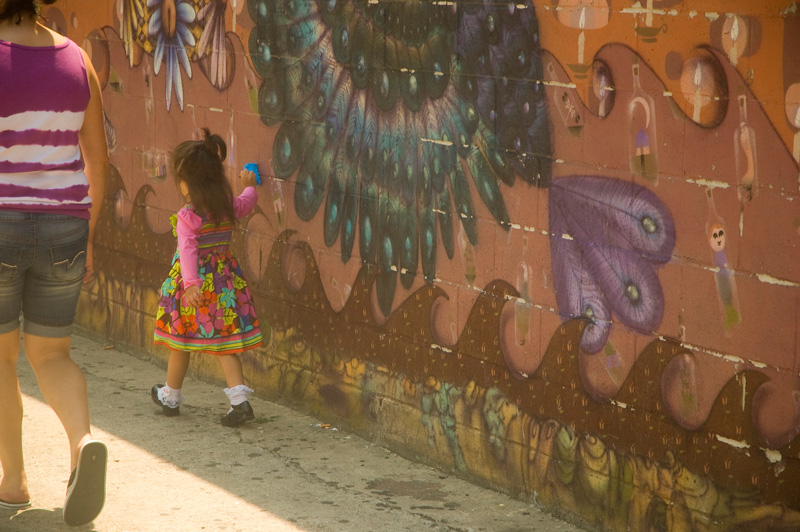 A little girl scrapes a toy on a wall with a mural