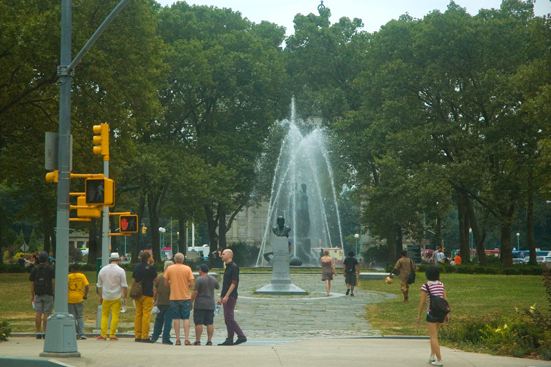 A plaza with people, water fountains, and sculptures.