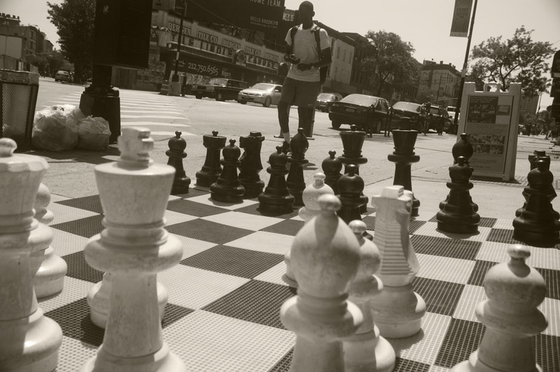 Pedestrian walking past a large plastic chess set.