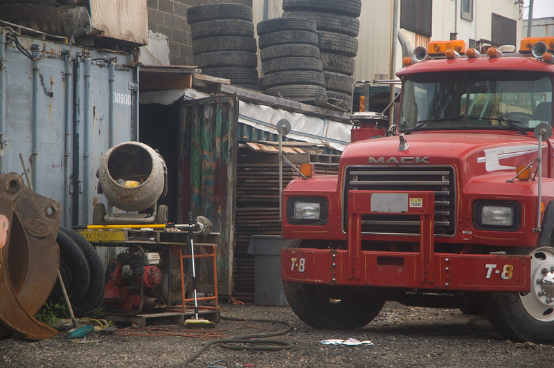 A truck yard, with a red Mack truck, tires, and a cement mixer.