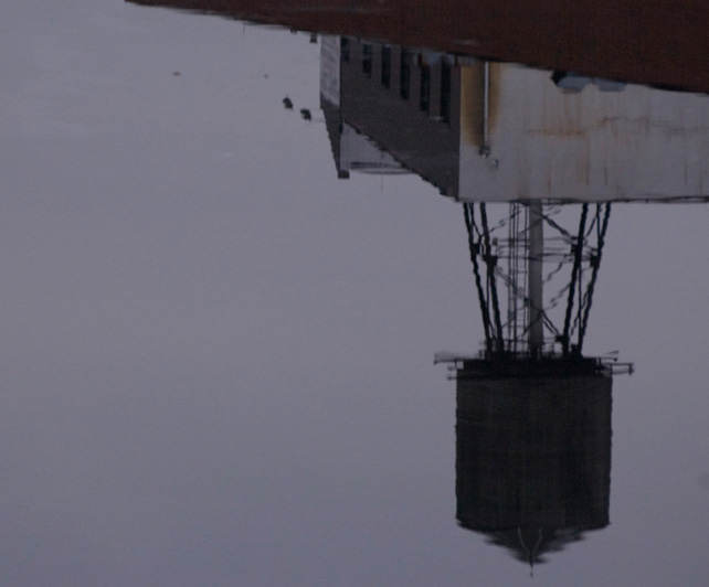 A water tank in silhouette, reflected in water