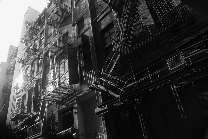 Sun streaks in a dark alley and fire escapes.