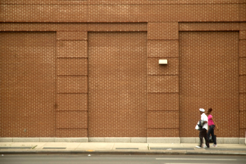 Two people walking past a massive brick wall.