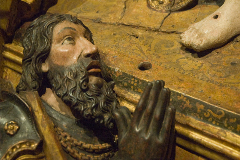 A sculpture of a man praying at the foot of Christ.