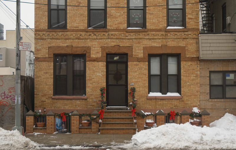 Christmas bows decorate a brick building, with snow.
