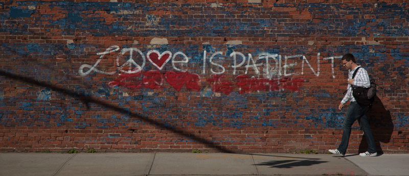 Man passing graffiti reading 'Love is Patient.'