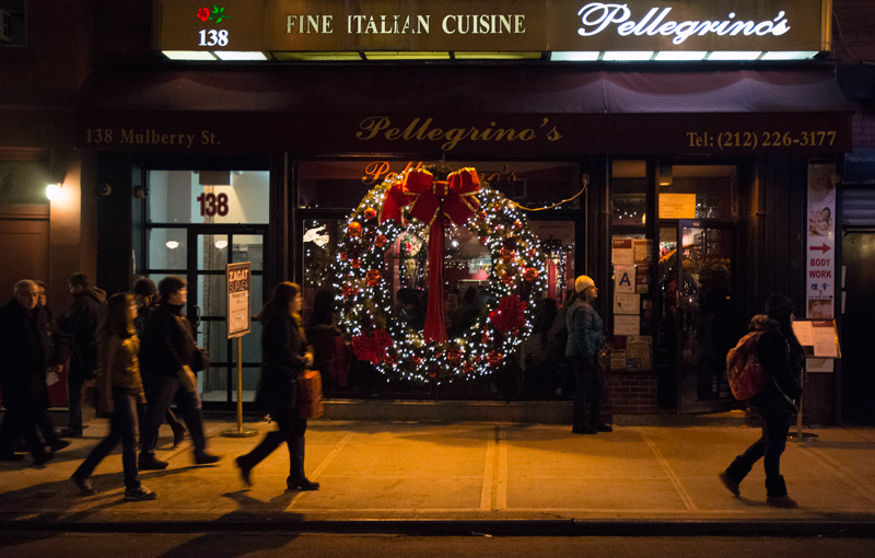 People pass a huge Christmas wreath in a restaurant's window.