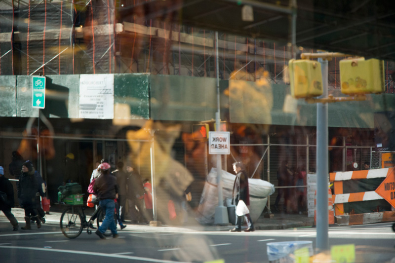 Window reflection of a man near a sign reading 'Work Ahead.'
