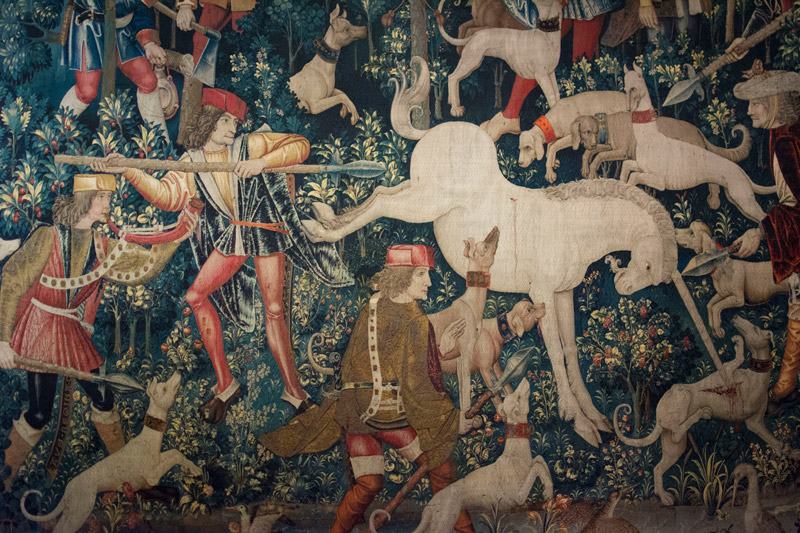 In a tapestry, a hunter prepares to spear a unicorn.