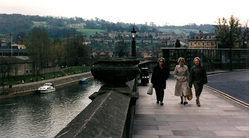 Three women walk along a river in Bath, England.