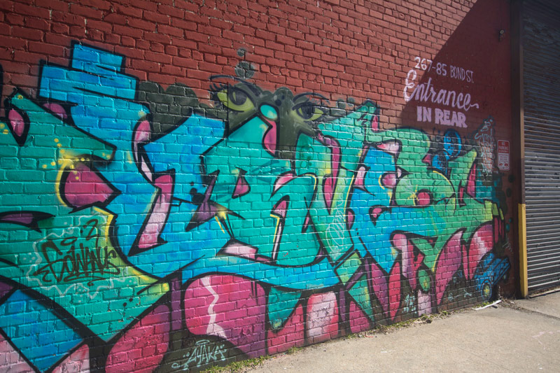 A wall covered with commissioned graffiti, and a message informing visitors the entrance is in the rear.