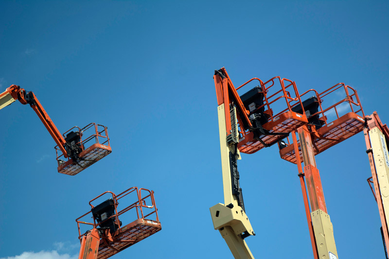 Cherry pickers atop cranes, against a blue sky.