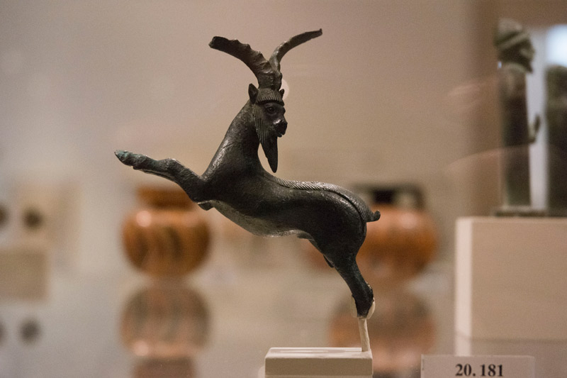 A small, bronze figure of a goat, rearing its front legs.