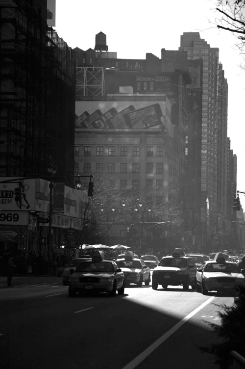 Taxi cabs caught in sunlight and shadows on an avenue.