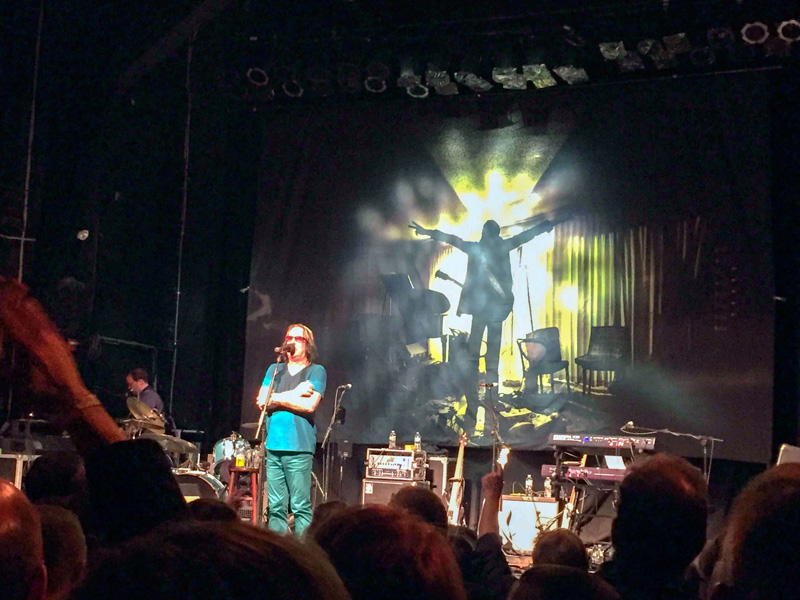 Todd Rundgren speaking at a concert.