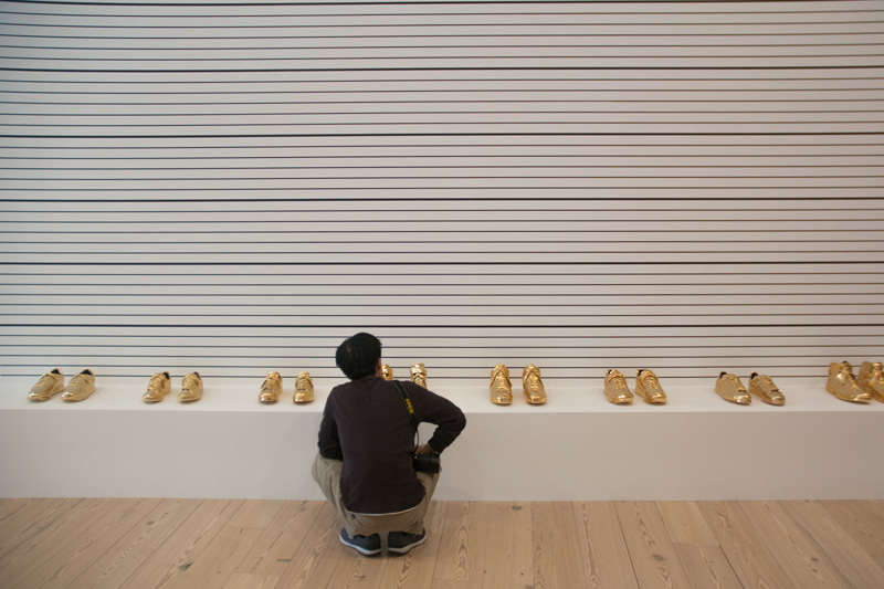 A museum visitor inspects gilded sneakers from a champion basketball team.