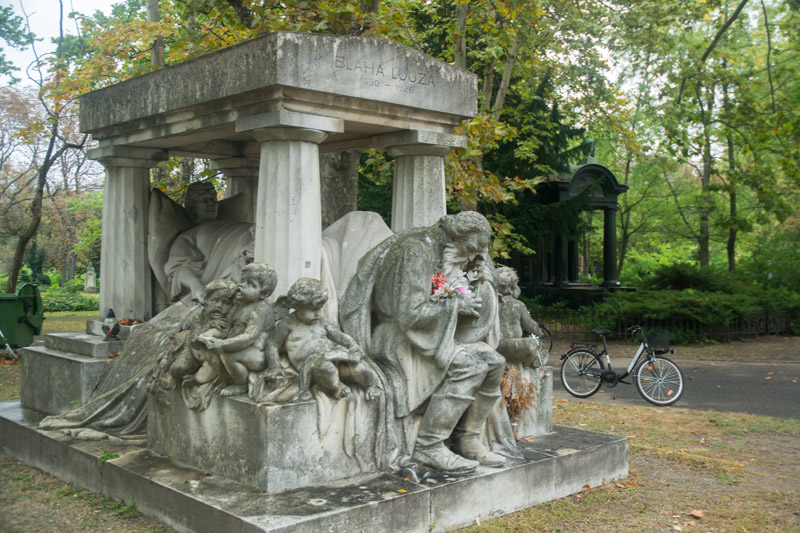 An elaborate grave, with a sculpture of deceased Lujza Blaha on her deathbed, surrounded by mourners.