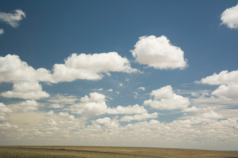 White clouds in a blue sky over a desert.