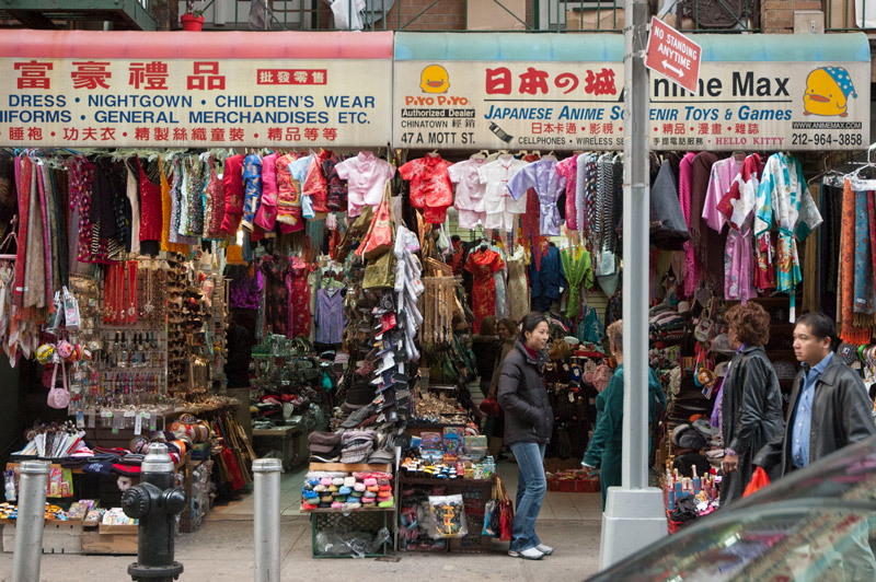 Two stores on a Chinatown street with packed-tight hangers of clothing.