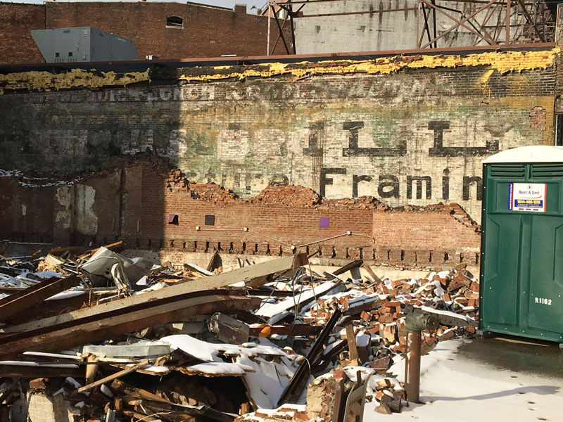 Demolition reveals a building wall with many layers of wall signs.