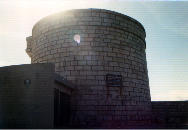 A round tower made of blocks, with a plaque
on its side designating its history.