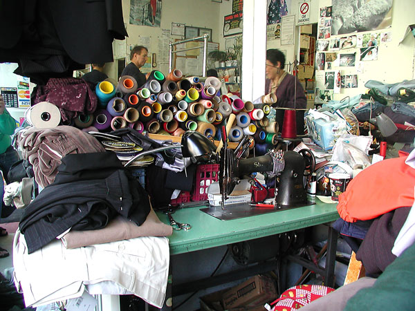 Many spools of colored thread sit on a counter
with a sewing machine and clothes waiting to be
altered.