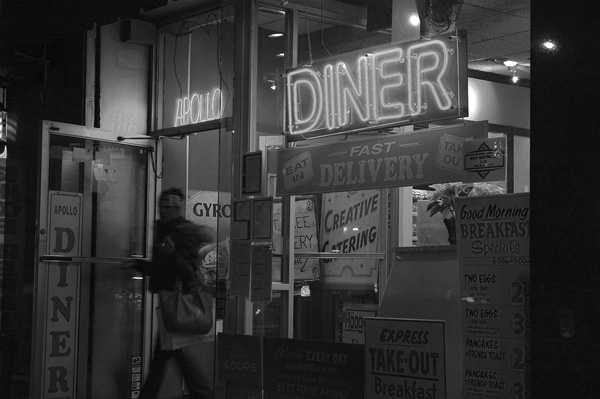A
woman exits the front door of a neon-lit diner