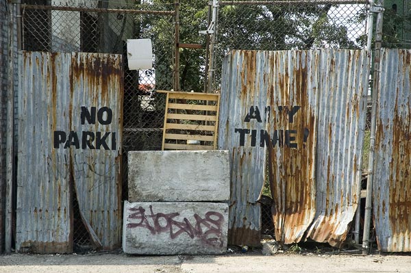 A sign on a rusty, corrugated metal wall says no parking
