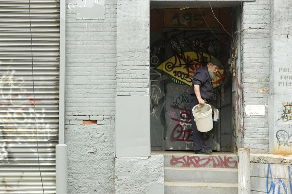 A man with bucket pauses at a door surrounded by graffiti