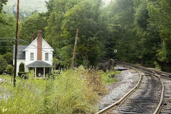 A house is on the left, and tracks curve into the woods.