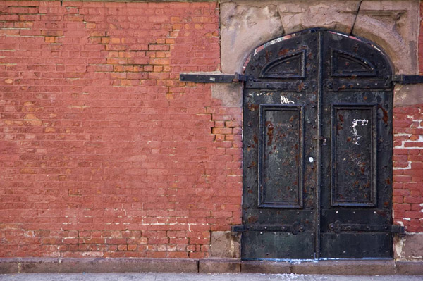 An old brick wall has old black iron doors.
