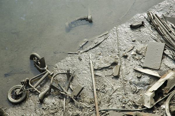 A bicycle and other trash partially submerged in mud.