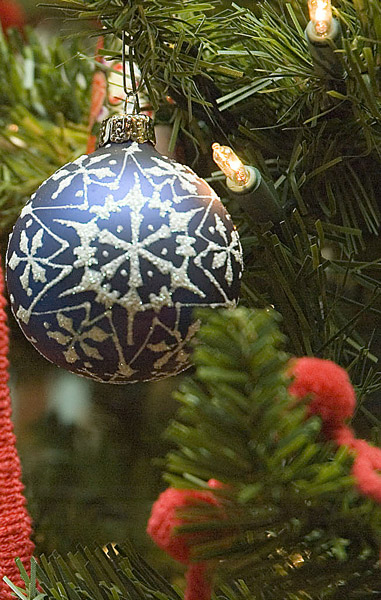 A blue, frosted ornament hangs amid red garland on
a Christmas tree.